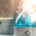Humidifier emitting a plume of visible mist on a bright windowsill next to a potted plant, illustrating indoor air quality control.