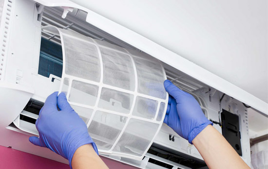 Technician wearing blue gloves removing or inspecting the clean air filter of a wall-mounted ductless AC unit.