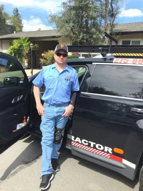 Precision Aire HVAC technician in a blue uniform standing by a black service truck with a ladder rack in a residential neighborhood.