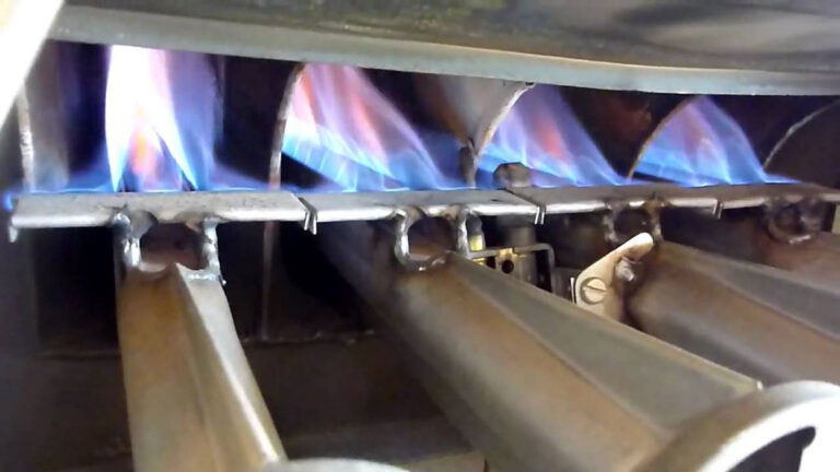 Close-up view of a gas furnace burner assembly showing multiple rows of clean, blue flames indicating efficient operation.